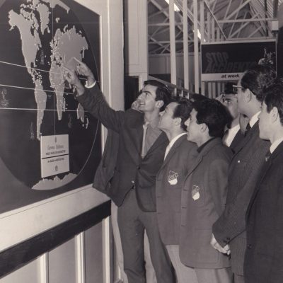 Μέλη της κυπριακής αποστολής μπροστά σε παγκόσμιο χάρτη, ο οποίος απεικονίζει την παραγωγή και τη διάθεση των προϊόντων της Εταιρείας Carreras Rothmans.